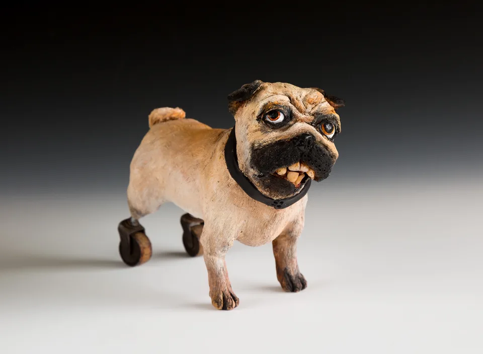 A small ceramic pug with an expressive face and found-object wheels.