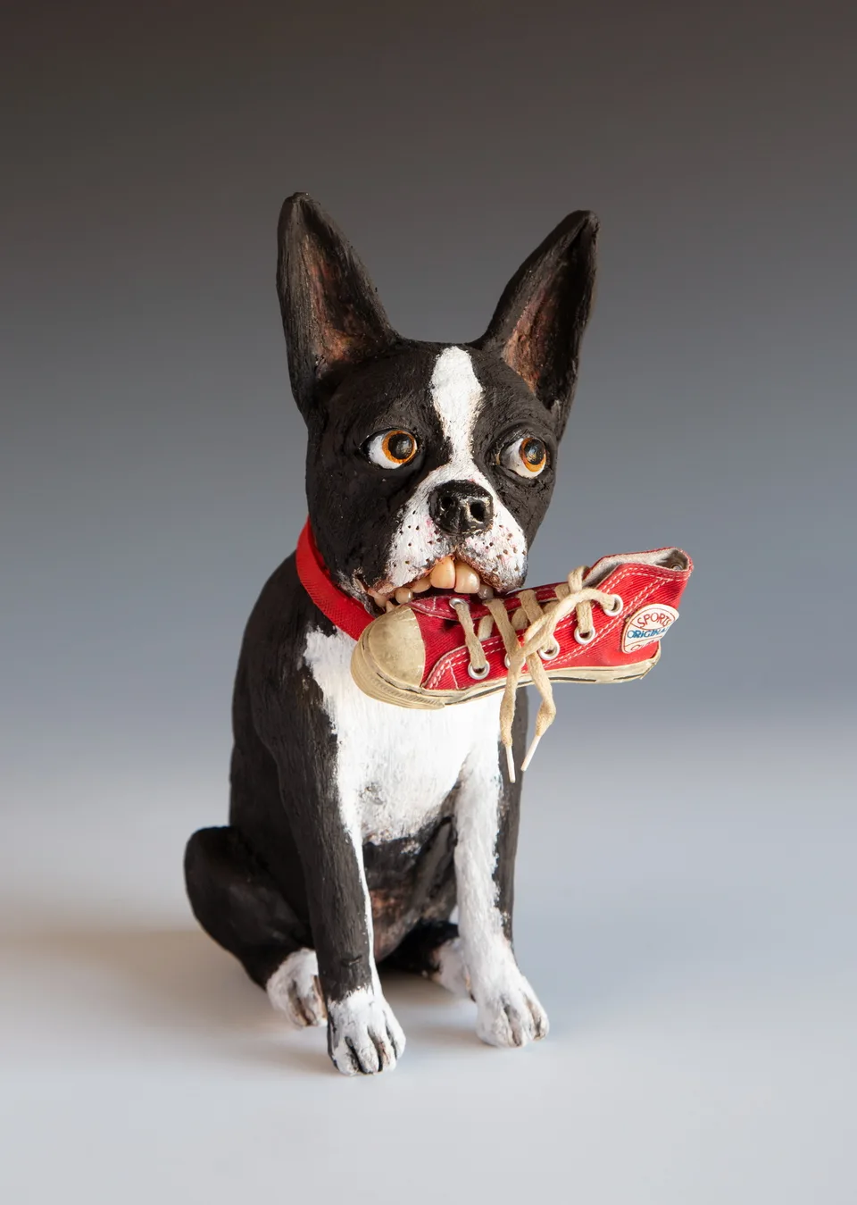 A black-and-white ceramic dog holding a red sneaker.